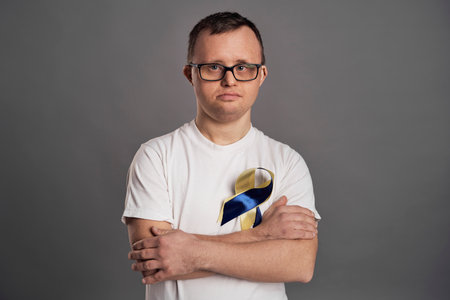 Portrait of man with down syndrome on gray background with yellow and blue bowの写真素材