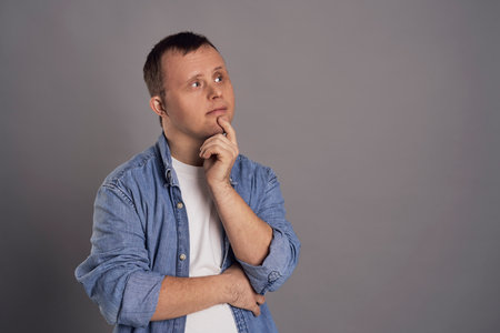 Man with down syndrome thinking about something on gray backgroundの写真素材