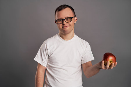 Man with down syndrome holding apple hands on gray backgroundの写真素材