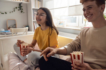 Two caucasian teenagers having fun while sitting on the floor and eating popcornの写真素材
