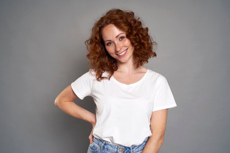 Portrait of red head caucasian woman wearing blue jeans and white tshirt on grey background