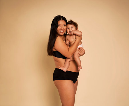 Portrait of cheerful Asian woman in underwear carrying a cute toddlerの写真素材