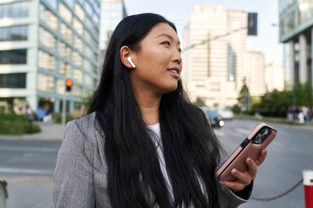 Business Chinese woman wearing earphones and calling on the streetの写真素材