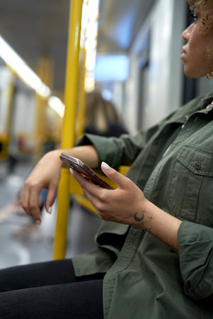 Vertical image of young afro woman traveling by underground and browsing a mobile phoneの写真素材