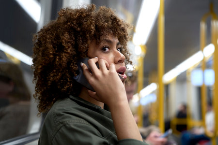 Young afro woman traveling by underground and talking on mobile phoneの写真素材