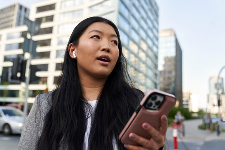 Business Chinese woman wearing earphones and calling on the streetの写真素材