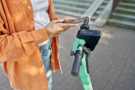 Unrecognizable woman using mobile phone to use a electric scooterの写真素材