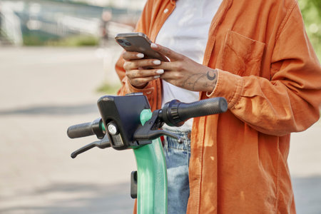 Unrecognizable woman using mobile phone to use a electric scooterの写真素材
