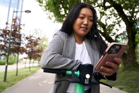 Chinese woman using mobile phone to use a electric scooterの写真素材