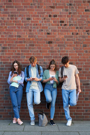 Group of university students browsing phones next to university campus buildingの写真素材