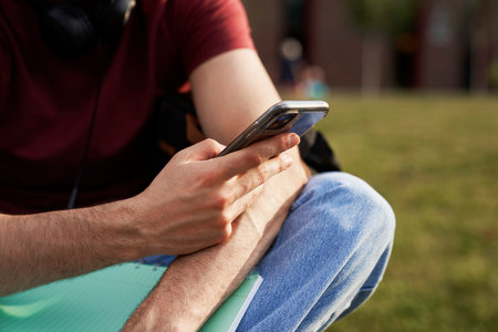 Unrecognizable student browsing phone while sitting on campusの写真素材