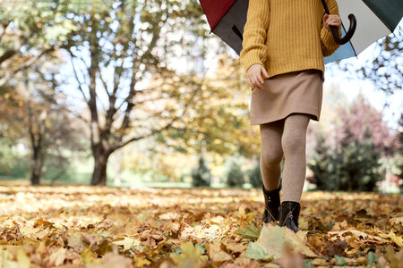 Low section of girl walking in the park and holding a colorful umbrellaの写真素材
