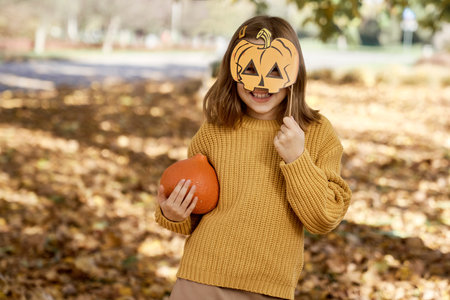 Portrait of girl standing in the woods and holding photo booth accessory and a pumpkinの写真素材