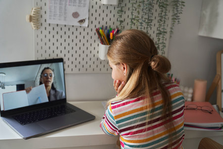 Caucasian elementary age girl having video conversation on laptop while sitting on the bedの写真素材