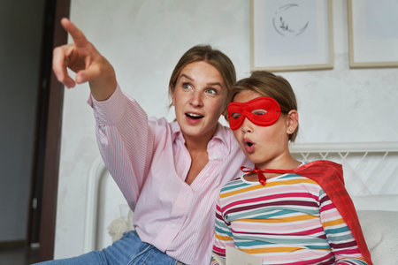 Caucasian mother and daughter in superhero outfit pointing awayの写真素材