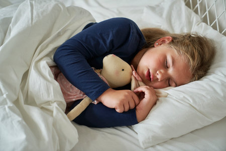 Little caucasian girl sleeping in bed with teddy bearの写真素材