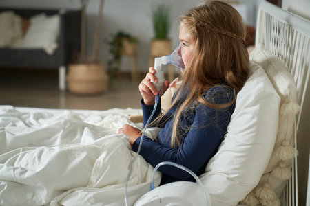 Elementary age girl using nebulizer in bed at homeの写真素材