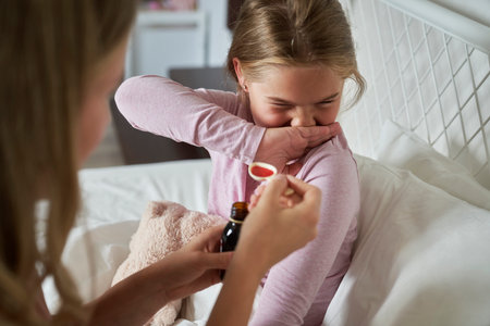Woman giving syrup to an ill girl sitting on bedの写真素材