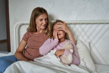 Mother talking to her ill girl child lying in bedの写真素材