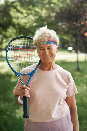 Portrait of senior woman standing in the park and holding tennis racketの写真素材