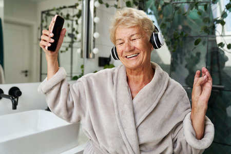 Senior caucasian woman using headphones and dancing in the bathroomの写真素材
