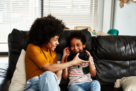 Siblings wearing virtual reality simulator to play video game in the living roomの写真素材