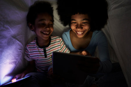 Two children browsing digital tablet at night under the duvetの写真素材