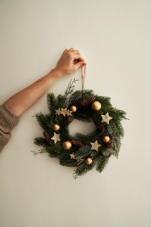 Vertical image of woman hanging a Christmas wreath on the wallの写真素材