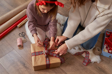 High angle view of caucasian girl and mother wrapping Christmas gifts on the floorの写真素材