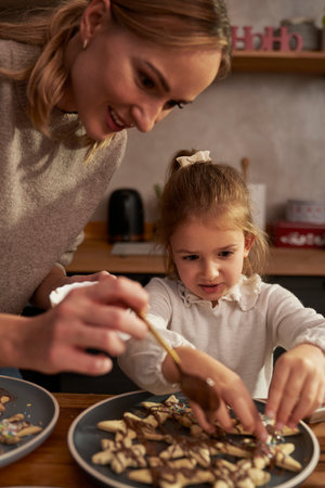Mother and daughter decorating gingerbreads with chocolate