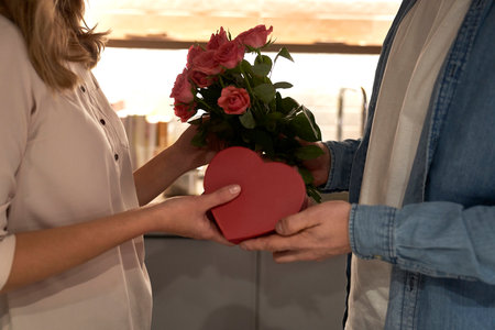 Man giving a box of chocolates and bunch of roses to his beloved woman