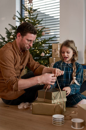 Father and daughter packing Christmas presents next to Christmas treeの写真素材