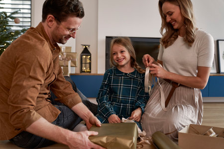 Family of three packing Christmas presents next to Christmas treeの写真素材