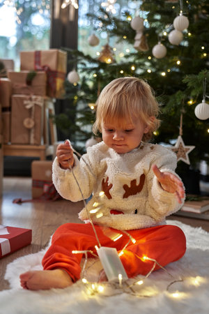 Toddler sitting on floor and playing with Christmas lightsの写真素材