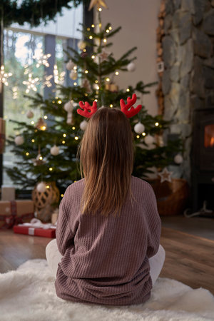 Rear view of girl wearing antlers and looking at Christmas treeの写真素材