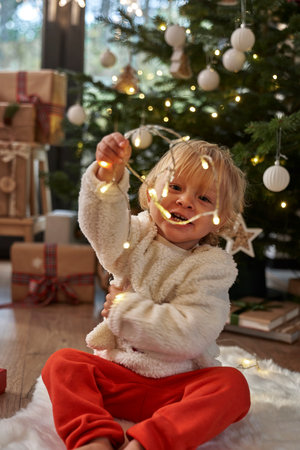 Toddler sitting on floor and playing with Christmas lightsの写真素材