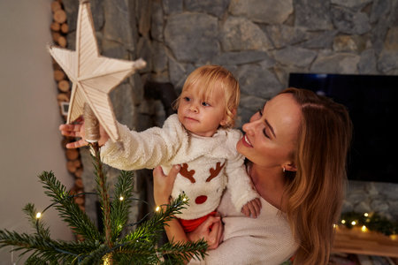 Mother carrying a toddler and standing next to the Christmas treeの写真素材