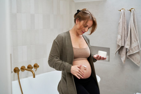 Caucasian pregnant woman applying moisturizer on her abdomenの写真素材