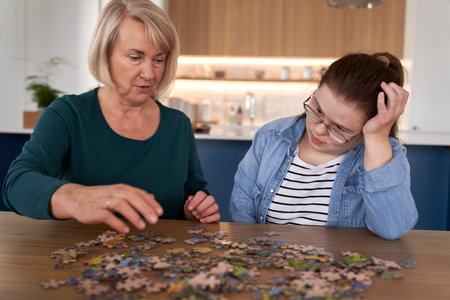 Focus down syndrome woman and her mother assembling puzzles at homeの写真素材