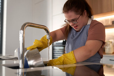 Down syndrome woman washing dishes in domestic kitchenの写真素材