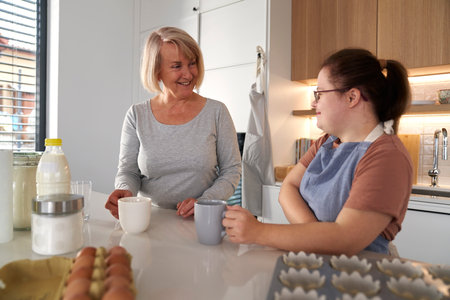 Down syndrome woman and her mother chatting in the kitchenの写真素材