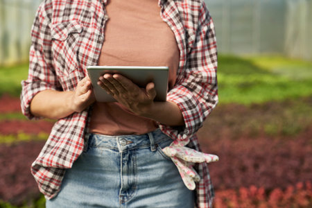 Caucasian female botanist standing in the greenhouse and using digital tabletの写真素材