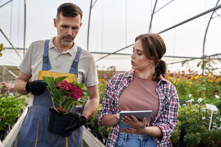 Two caucasian botanists standing in the greenhouse and using digital tabletの写真素材