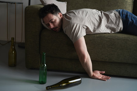 Drunk man lying on sofa among empty bottlesの写真素材
