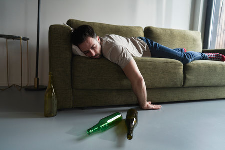 Drunk man lying on sofa among empty bottles
