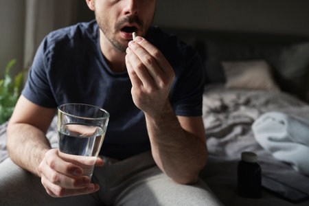Man sitting on bed and taking pillsの写真素材
