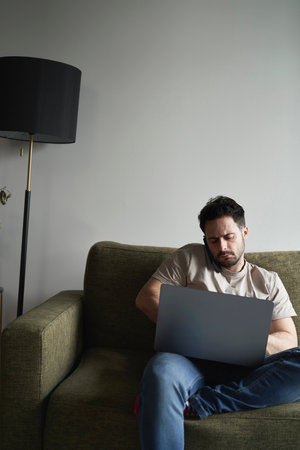 Man using laptop and calling while sitting on sofaの写真素材
