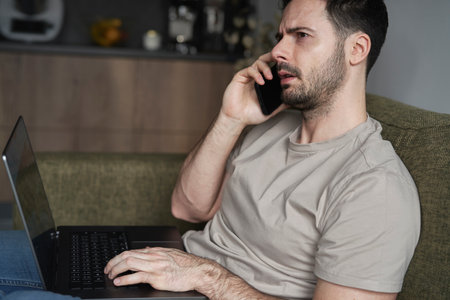 Man using laptop and calling while sitting on sofaの写真素材