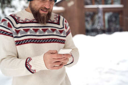Close up of caucasian man using mobile phone in front of wooden house in winterの写真素材