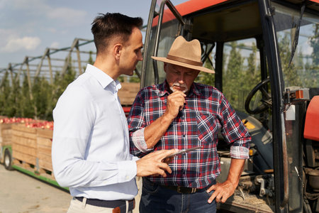 Senior farmer and sales representative talking over digital tablet on apple orchardの写真素材